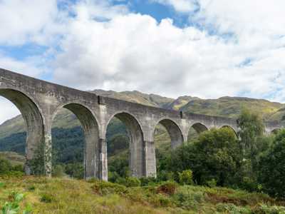 tall stone arches of Glenfinnan Viaduct with lush scenery in the background
