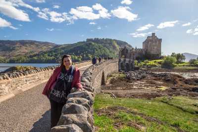 Long stone bridge leading up to Eilean Donan Castle with stone wall architecture and forested hills in the background