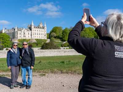 HIghland Explorer Tours guide taking a photo of two travellers before Dunrobin Castle