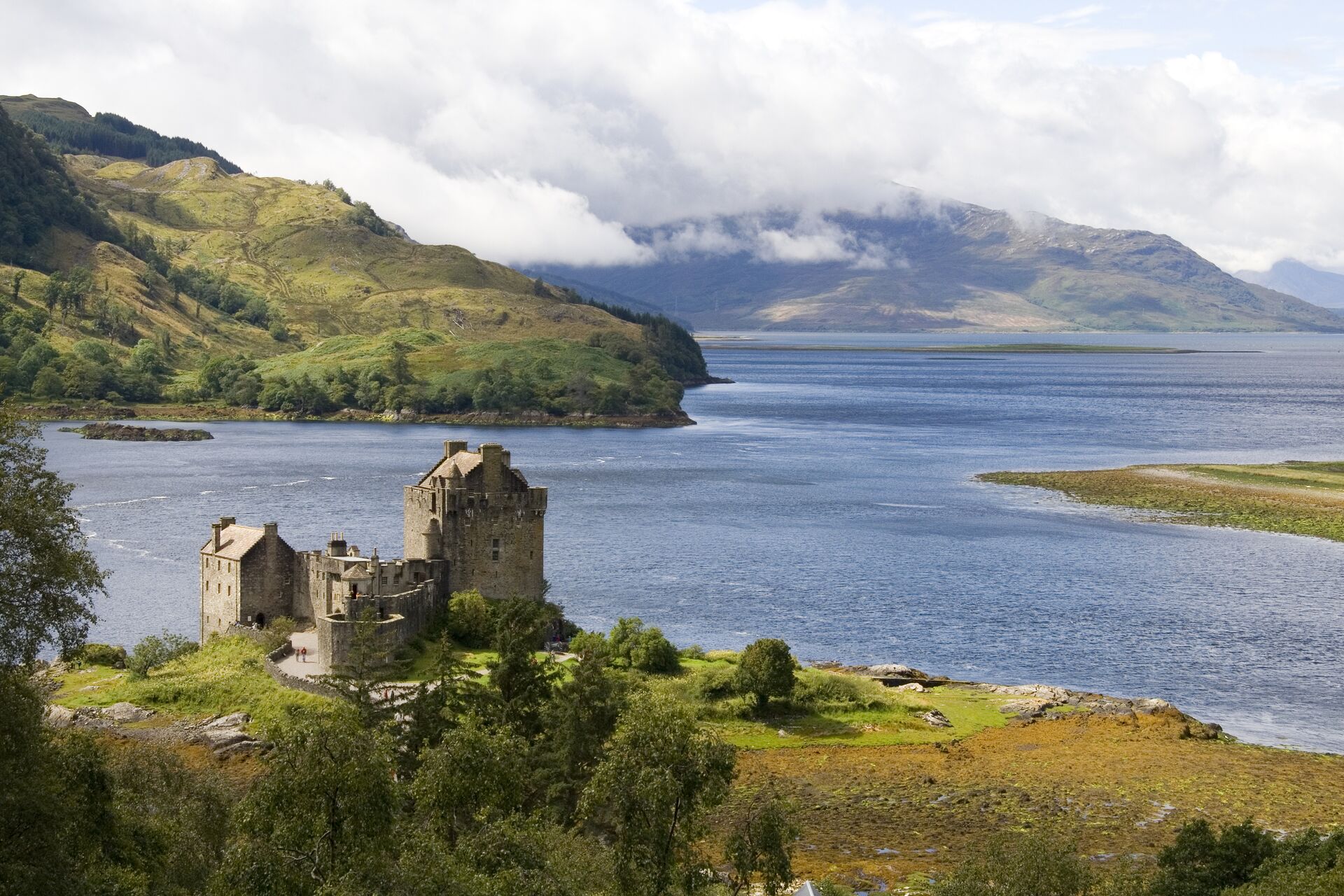 Aerial view of Eilean Donan Castle surrounded by sea loch and mountain backdrop