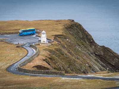 Blue Highland Explorer bus parked at Sumburgh Head Lighthouse in Shetland, with the rugged coastline and the North Sea