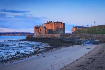 Blackness Castle nestled on beach with stone wall set against dramatic blue and pink skies during sunset