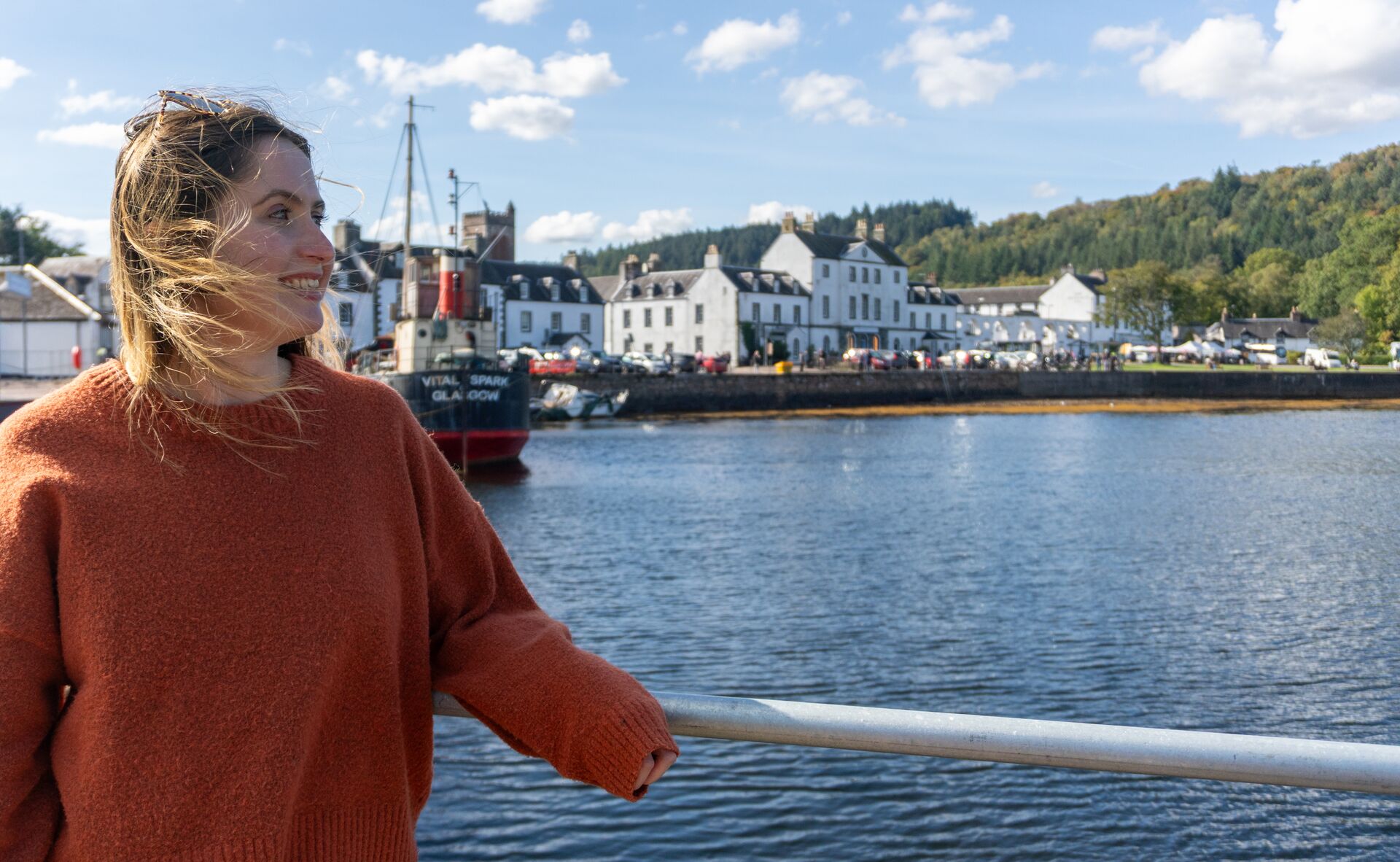 Young woman standing at Inveraray's pier with the white stone building of the village in the background