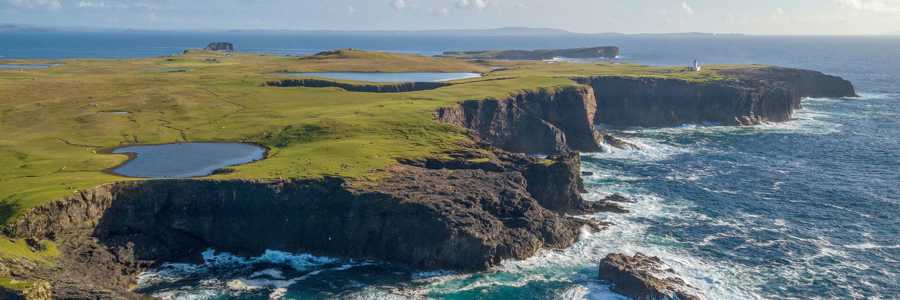 Eshaness coast on Shetland with rugged cliffs and crashing waves, illuminated by bright sunshine