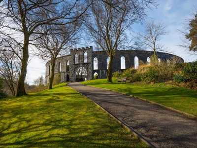 MacCaigs Tower in Oban, an arched stone monument surrounded by trees and lush lawn
