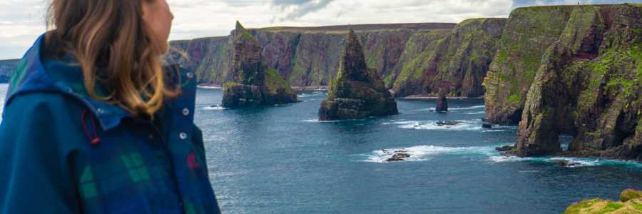Woman looking at the impressive coastal formations of Duncansby Head