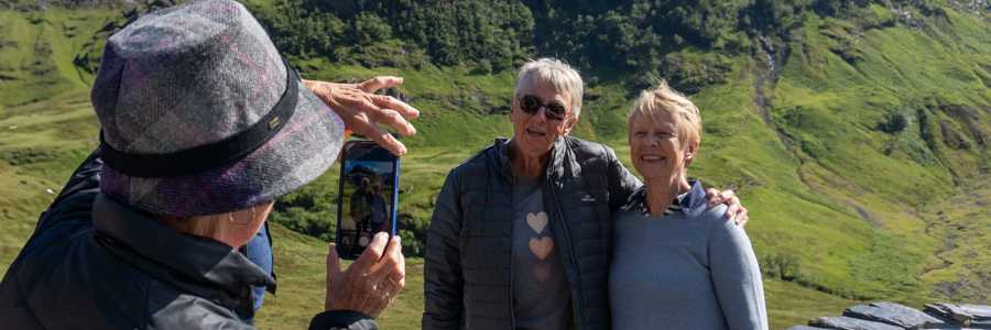 Traveller taking a photo oftwo friends before the striking valley of Glen Coe