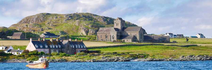 View of Iona Abbey from the water, with green hills on the island under a sunny sky