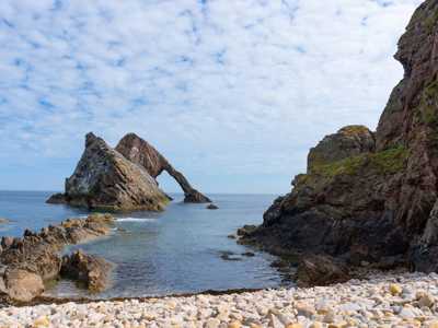 Bow Fiddle Rock, a unique sea arch on the Moray coast, illuminated by sunlight with clear blue skies and the ocean below