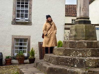 Young woman admiring a tall stone monument in Culross Village