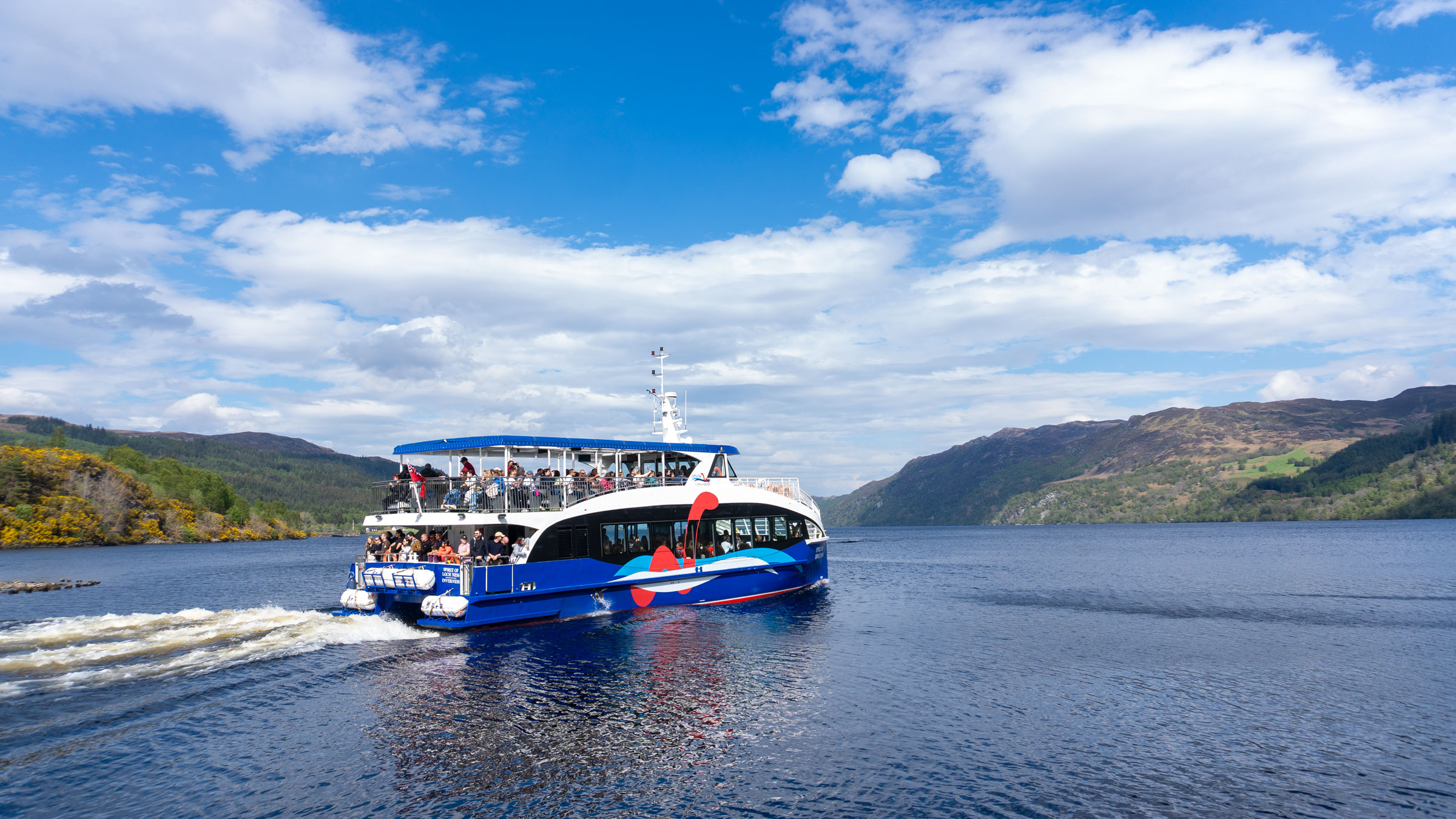 Small Loch Ness boat cruise travelling on the waters of Loch Ness under blue skies
