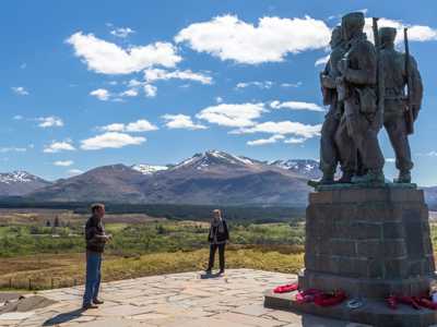 Two travellers admiring the impressive statue of Commando Memorial against the backdrop of Ben Nevis mountain