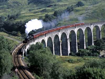 Jacobite Steam Train crossing the iconic Glenfinnan Viaduct, surrounded by lush greenery