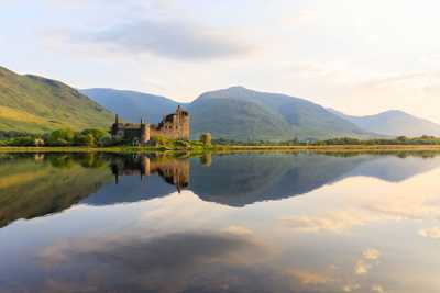Ruins of Kilchurn Castle sitting on a lake surrounded by green hills