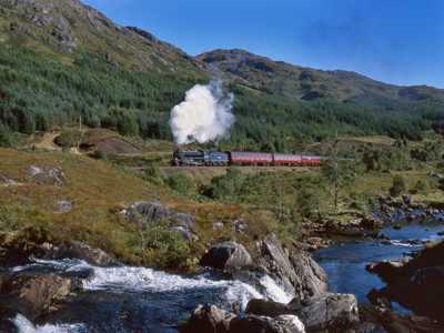 Jacobite Steam Train with red carriages travelling through forested area with river